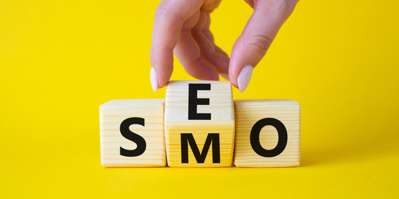 A businessman turns wooden cubes and changes the word SMO to SEO, illustrating the SEO vs SMO concept.